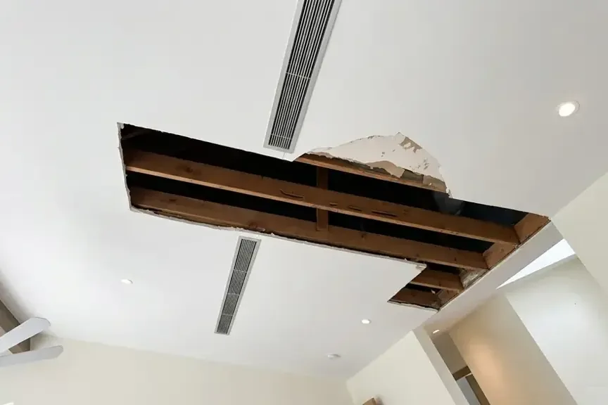 Ceiling drywall cut away to expose wet joists after a leak from above